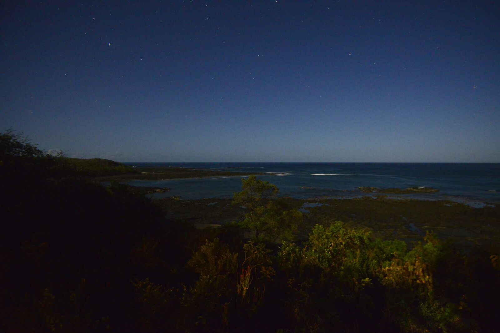 Paisaje costero nocturno con vista al océano y la costa lejana.