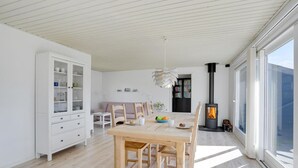 Een moderne woonkamer met een eethoek, een witte kast, een bank en een houtkachel.