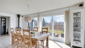 Een eetruimte met een houten tafel en stoelen, een moderne hanglamp en uitzicht op de omgeving door grote ramen.