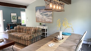 A living room with a plaid sofa, a wooden dining table, a woven placemat, and a vase with yellow flowers.