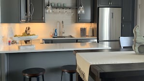 A modern kitchen with dark cabinets, a stainless steel refrigerator, and a central island with stools.