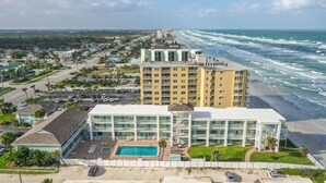 A hotel with multiple floors, a swimming pool, and a view of the ocean.