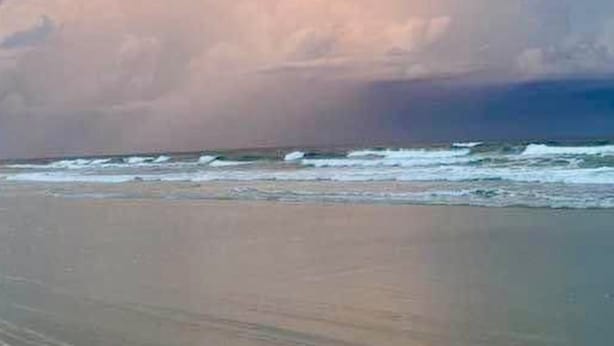 A beach with waves and a cloudy sky.