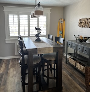 A dining area with a wooden table, four chairs, a decorative fish sculpture, and a surfboard on the wall.
