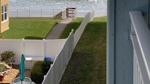 A balcony with a view of the ocean, a grassy area, and a white fence.
