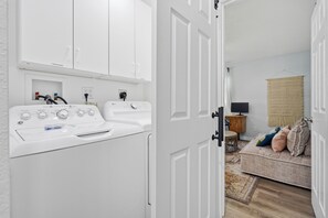 Un espace buanderie comprenant un lave-linge et un sèche-linge à chargement frontal, un chauffe-eau et une prise électrique murale.