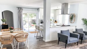 A modern kitchen with white cabinets, a stainless steel range hood, and a dining area with wicker chairs and a wooden table. - 🔆Clearwater Coastal Cottage🔆 newly renovated, near beaches & downtown Dunedin (Clearwater)