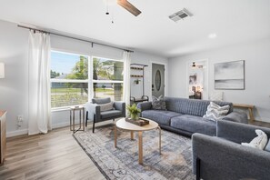 A modern living room with a grey sofa, a small round table, and a large window with blinds.