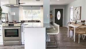 A modern kitchen with a central island, stainless steel appliances, and a dining area with wicker chairs. - 🔆Clearwater Coastal Cottage🔆 newly renovated, near beaches & downtown Dunedin (Clearwater)