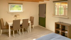 A small, well-lit room with a wooden floor, a desk with chairs, a bed, and a window with a view of greenery. - Cozy home in Tiendeveen with WiFi (Tiendeveen)