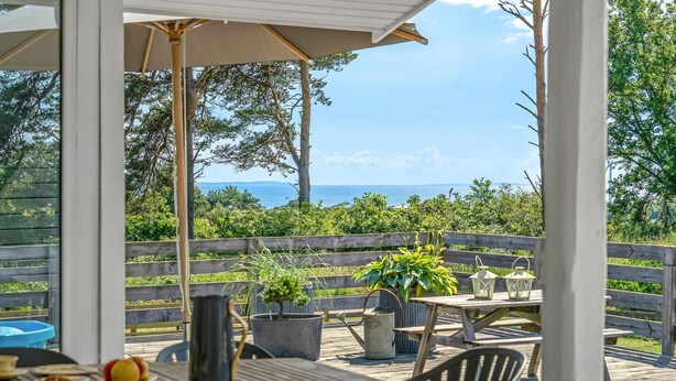Un espacio cubierto para comer al aire libre con vista al mar, mobiliario de madera y plantas en macetas.