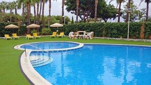 A swimming pool with a curved edge, surrounded by green grass and yellow lounge chairs.