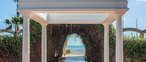 Una pérgola blanca con columnas que da a vista de la playa.