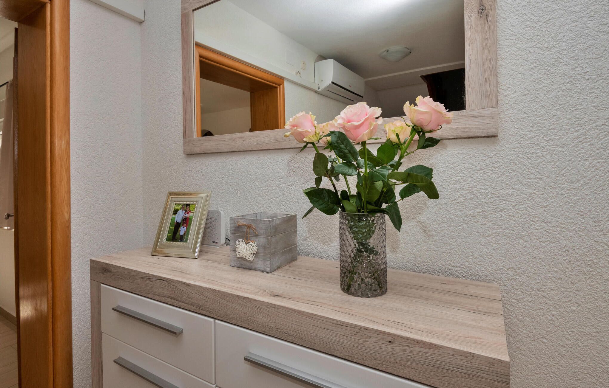 A bathroom vanity with a mirror, a vase with flowers, a framed photo, and a speaker.