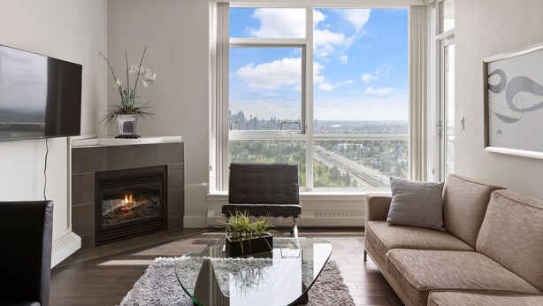 A modern living room with a fireplace, a sofa, a coffee table, and a large window offering a city view. - Newly Furnished 2BD, 2BA Condo with Pool and Stunning View! (Calgary)