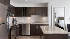 A modern kitchen with dark cabinetry, stainless steel appliances, and a granite countertop. - Newly Furnished 2BD, 2BA Condo with Pool and Stunning View! (Calgary)