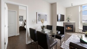 A modern living room with a glass-top dining table, black leather chairs, a fireplace, and a city view. - Newly Furnished 2BD, 2BA Condo with Pool and Stunning View! (Calgary)