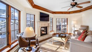 A spacious living room with a fireplace, large windows, and a ceiling fan. - Heart of Vail Village - Free Breakfast, Free Parking, No Resort Fee - Walkable (Vail)
