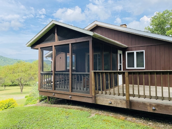A wooden cabin with a covered porch and a view of a green landscape.
