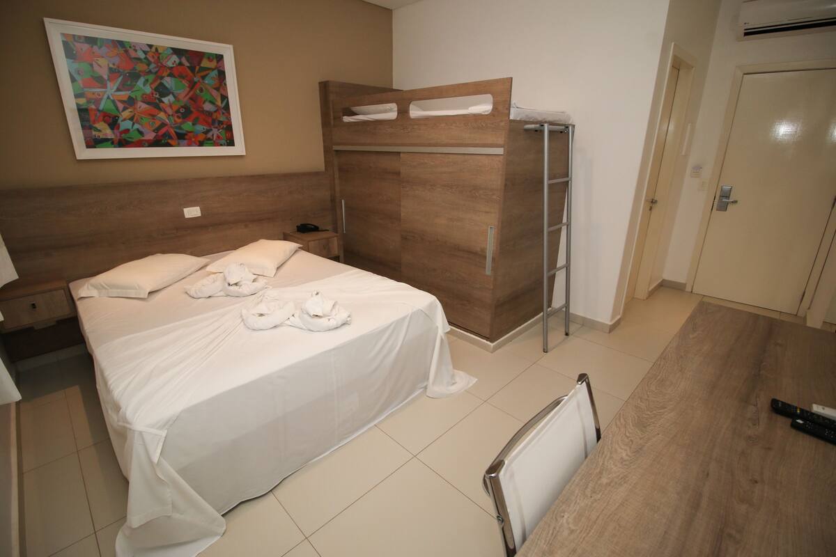 Une chambre d’hôtel avec un lit, une armoire en bois, un tableau au mur et une porte.