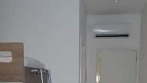 A room with a wooden wardrobe, a ladder, a desk, and a door leading to another room.