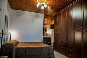Una camera da letto con soffitto in legno, un letto con copriletto marrone, un armadio e un lampadario.