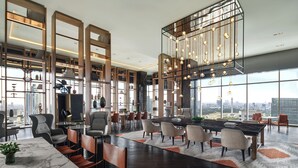 Uma área de estar ampla e moderna, com uma grande mesa de jantar, assentos confortáveis e vista para a cidade através de grandes janelas.