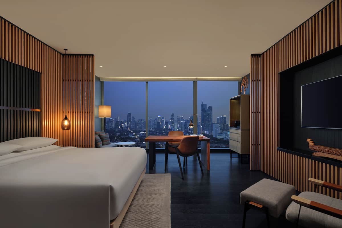 Una habitación de hotel moderna con una cama grande, un comedor y vistas a la ciudad.