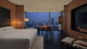A modern hotel room with a large bed, a dining area, and a city view.