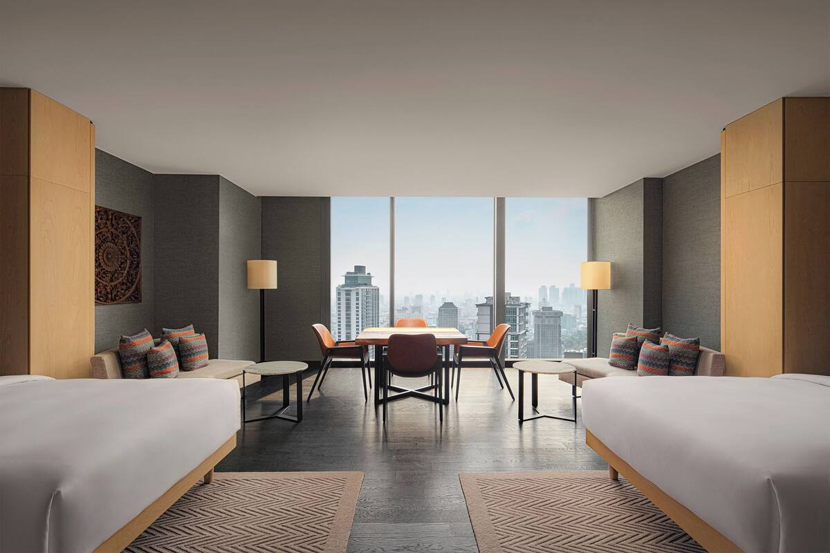 Habitación de hotel moderna con dos camas, una mesa de comedor, sillas y vistas a la ciudad.