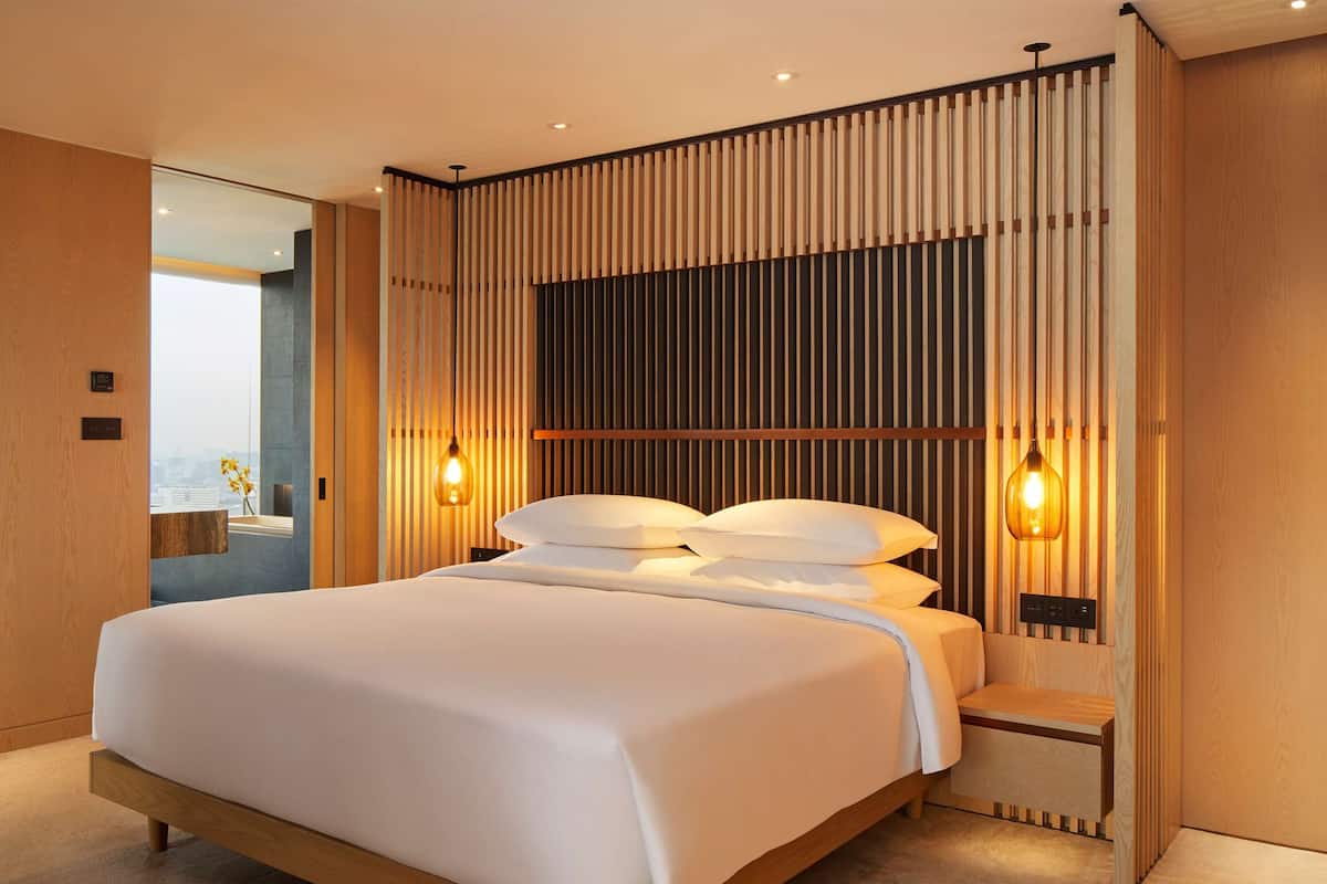Un dormitorio moderno con una cama grande, paneles de madera y dos lámparas fijadas a la pared.