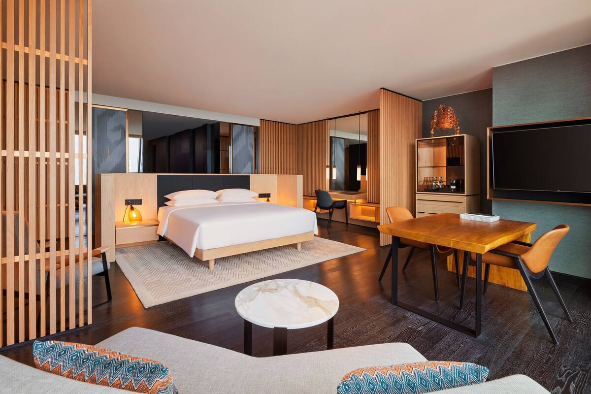 Una habitación de hotel moderna con cama, zona de comedor, televisor y espacio para sentarse.