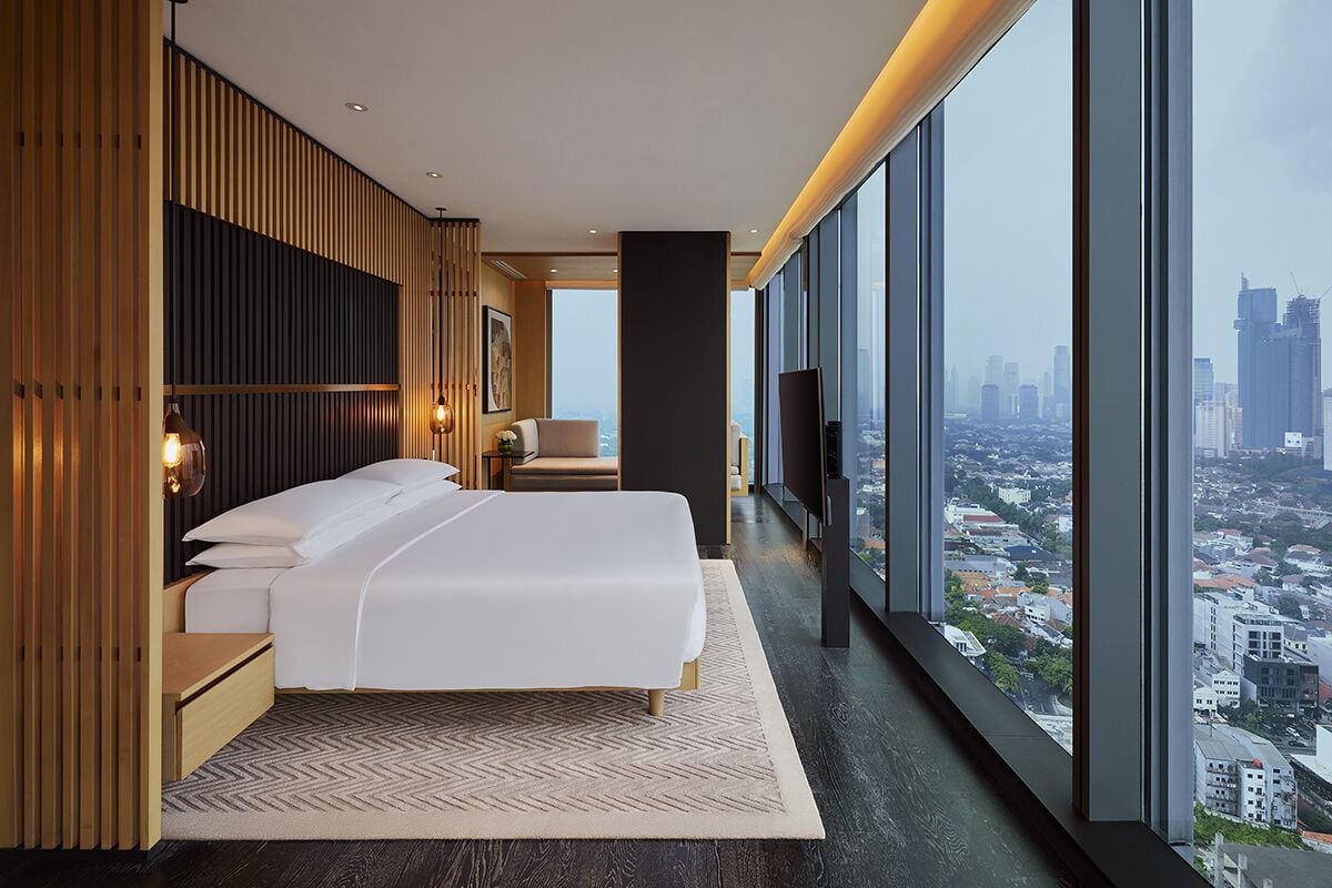 Habitación de hotel moderna con una cama grande, vistas a la ciudad y una pared decorativa de madera.