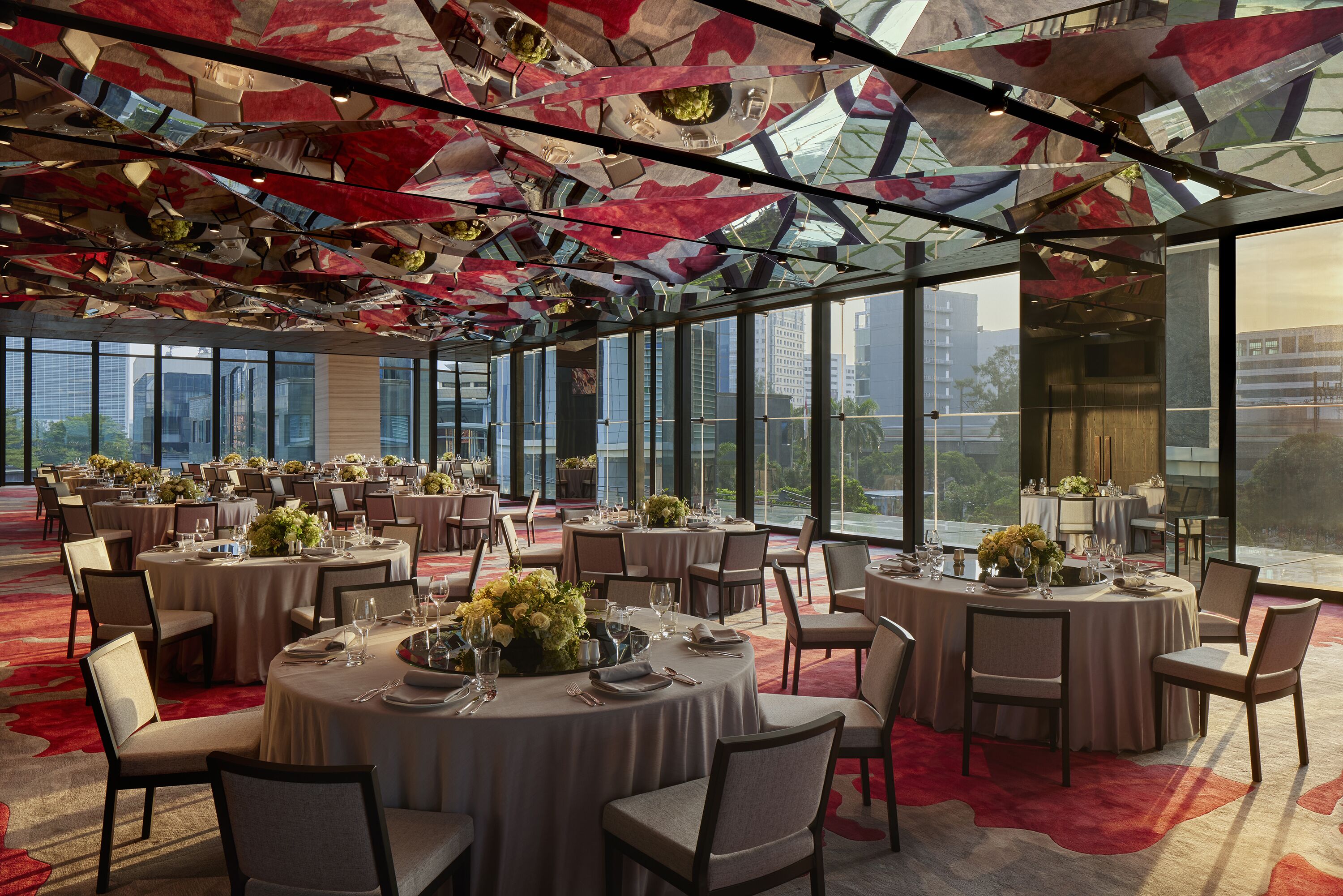 Un amplio salón de banquetes con mesas redondas, sillas y un techo con paneles reflectantes.