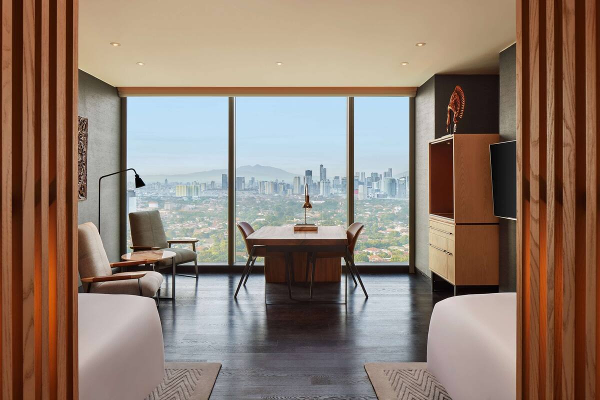 Habitación de hotel moderna con amplia vista de la ciudad, una mesa de comedor de madera, asientos cómodos y un televisor de pantalla plana.