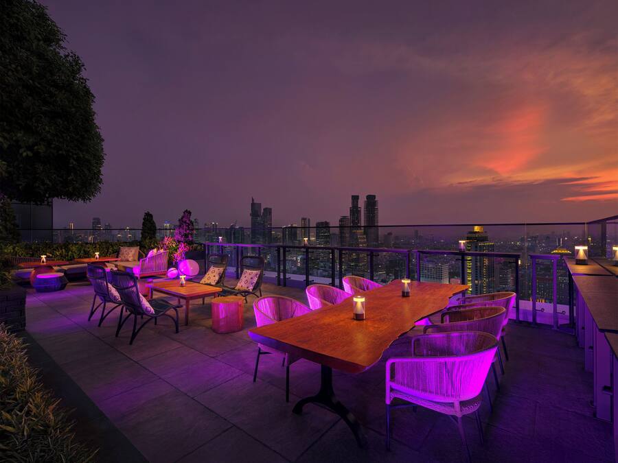 Terraza al aire libre con vistas a un horizonte urbano, con una mesa y sillas de madera, e iluminación ambiental.