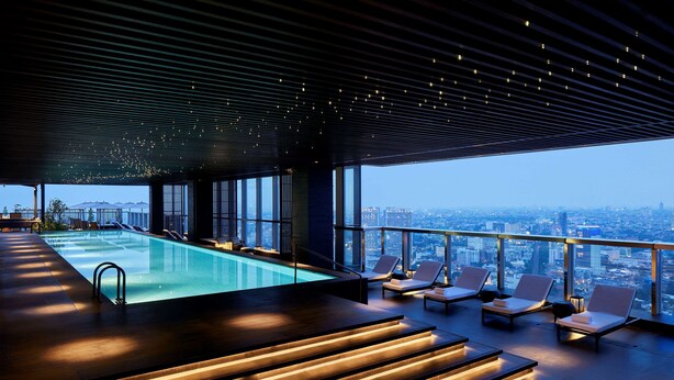 A rooftop infinity pool with lounge chairs and a city view.