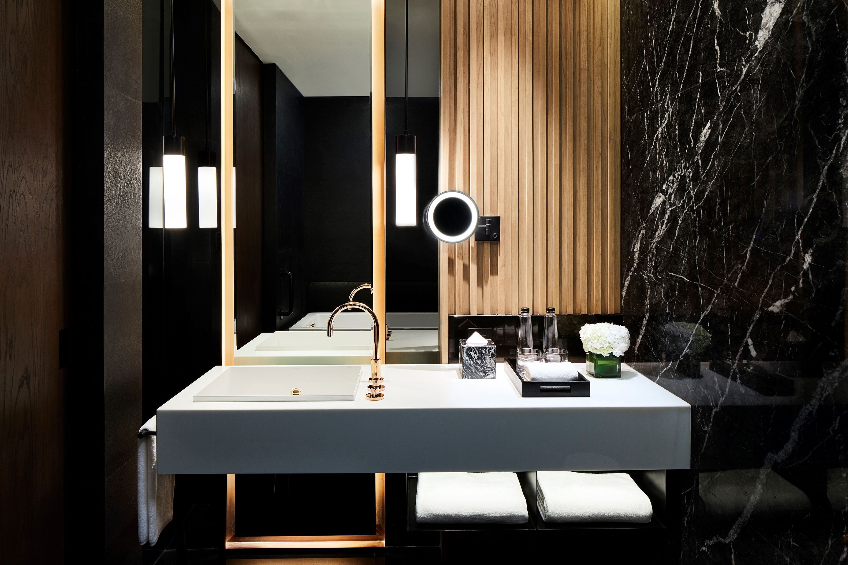 Un baño moderno con un lavabo blanco, un espejo con luz de aro y una pared de paneles de madera.