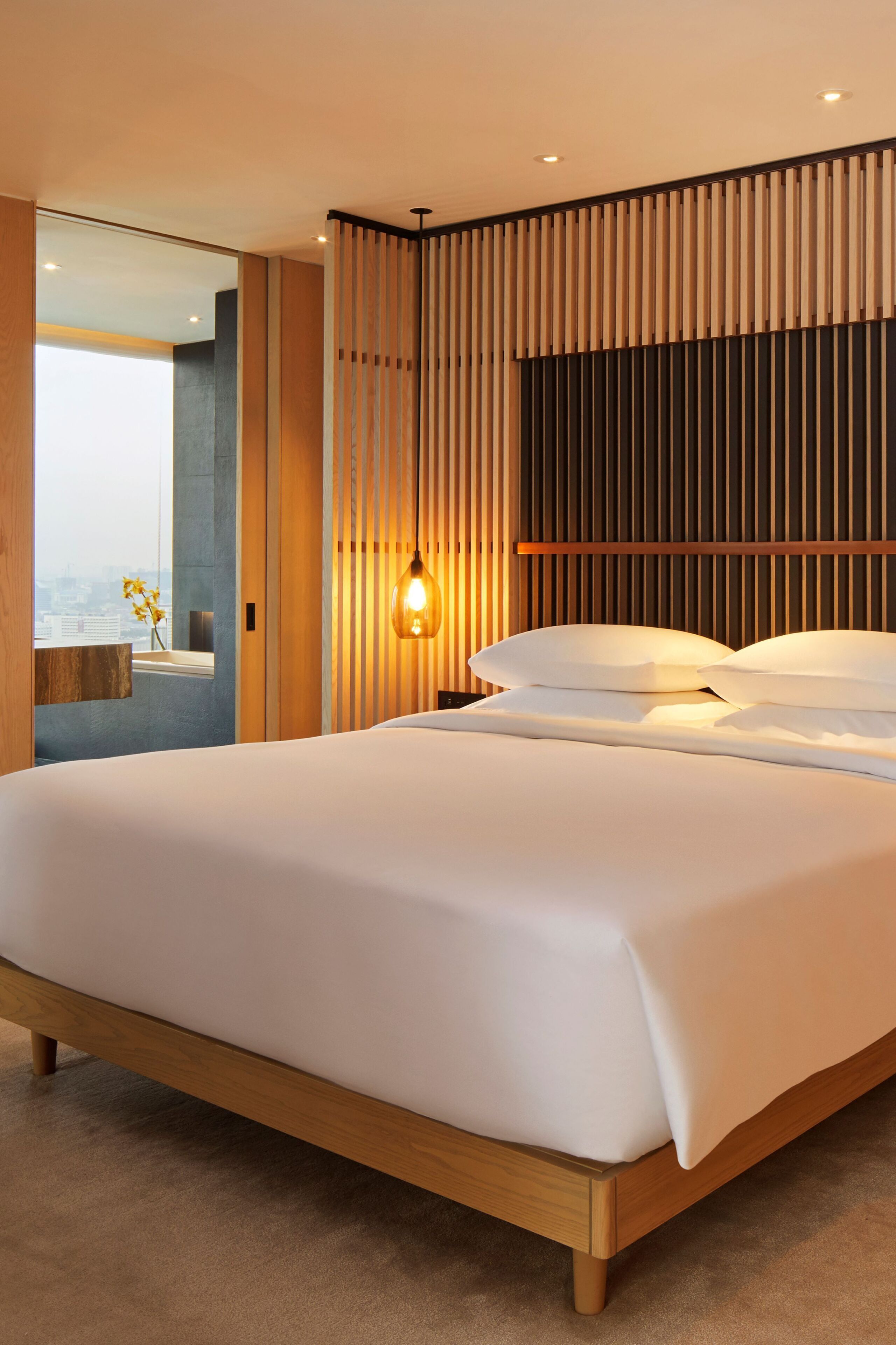 Un dormitorio moderno con una cama grande, cabecera de madera y vista a la ciudad a través de un ventanal.