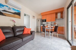 Moderni keittiö, jossa on oranssit kaapit, ruokapöytä tuoleineen, jääkaappi ja mikroaaltouuni.