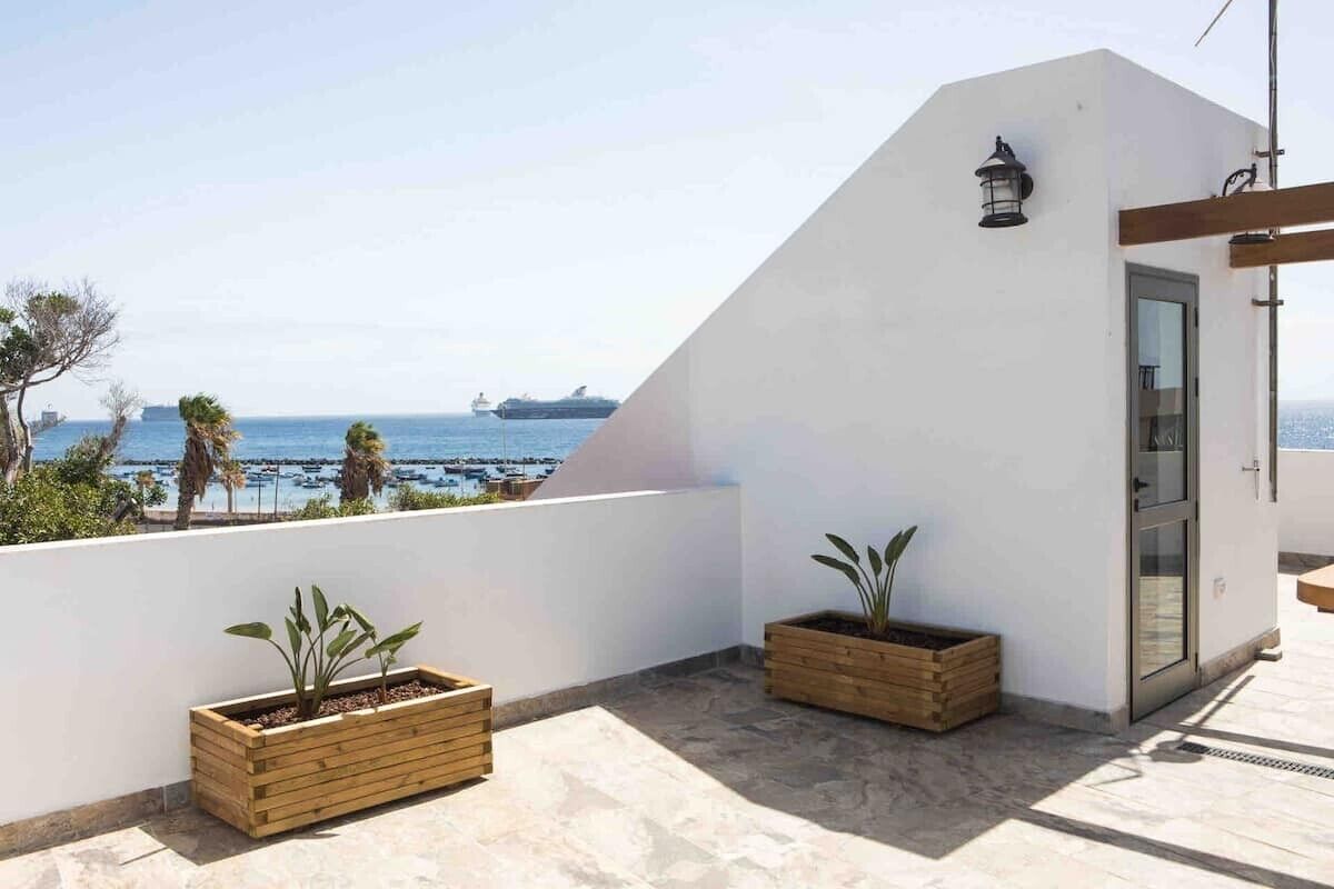 A rooftop terrace with a view of the sea, wooden planters, and a door.