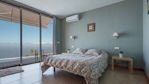 A bedroom with a bed, a nightstand, a lamp, a picture frame, and a view of the sea. - Holiday Home ‘Casa Santa Úrsula’ with Sea View, Pool, Wi-Fi & Garden (Santa ursula)