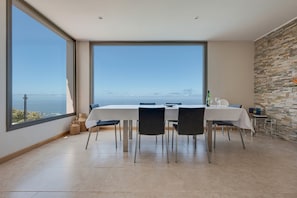 A dining area with a large table, chairs, and a view of the sea.
