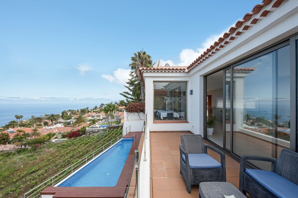 Un balcon avec une piscine, des meubles en osier et une vue sur la mer et les maisons.
