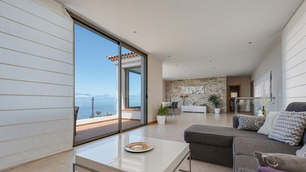 A modern living room with a glass door leading to a balcony, a sofa, a coffee table, and a stone accent wall. - Holiday Home ‘Casa Santa Úrsula’ with Sea View, Pool, Wi-Fi & Garden (Santa ursula)