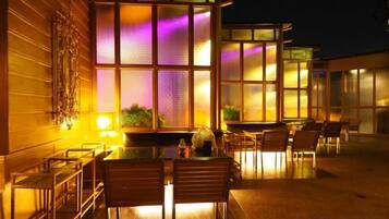 An outdoor seating area with tables and chairs, a building with large windows, and a decorative wall.
