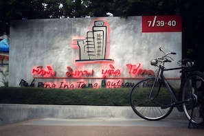 A sign with a building illustration and text, a bicycle, and a time display. - Pak Ping Ing Tang Boutique Hotel (Nonthaburi)