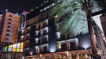 A multi-story hotel with balconies, a palm tree, and parked cars.
