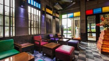 A cozy indoor seating area with wooden tables and chairs, large windows, and a checkered floor.