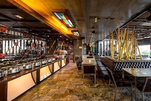 A restaurant interior with a stone floor, metal counters, and a seating area with tables and benches. - Pak Ping Ing Tang Boutique Hotel (Nonthaburi)
